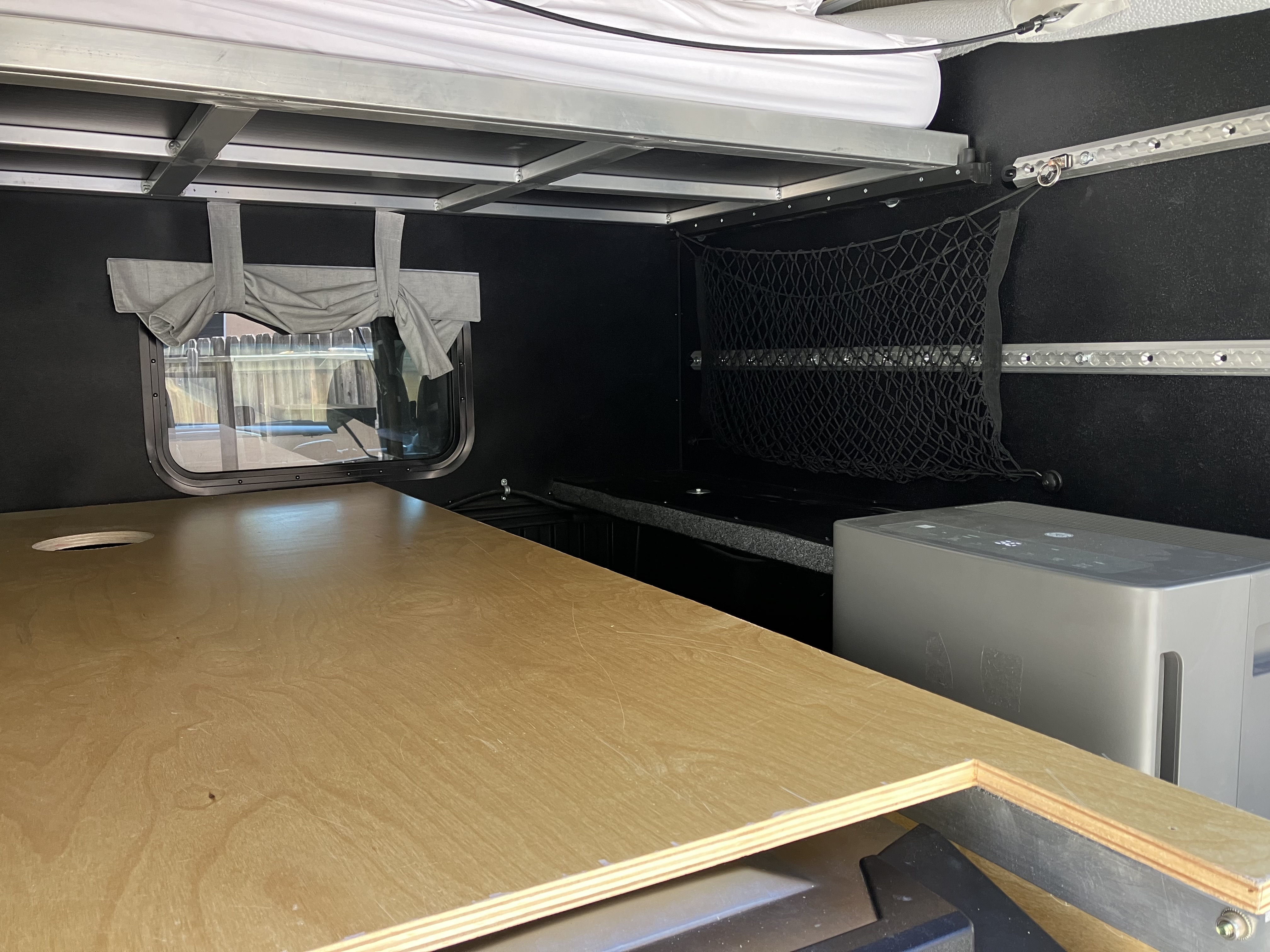 Lower interior view from the rear showing the third bed platform, side-window curtain, storage net, and GE dehumidifier