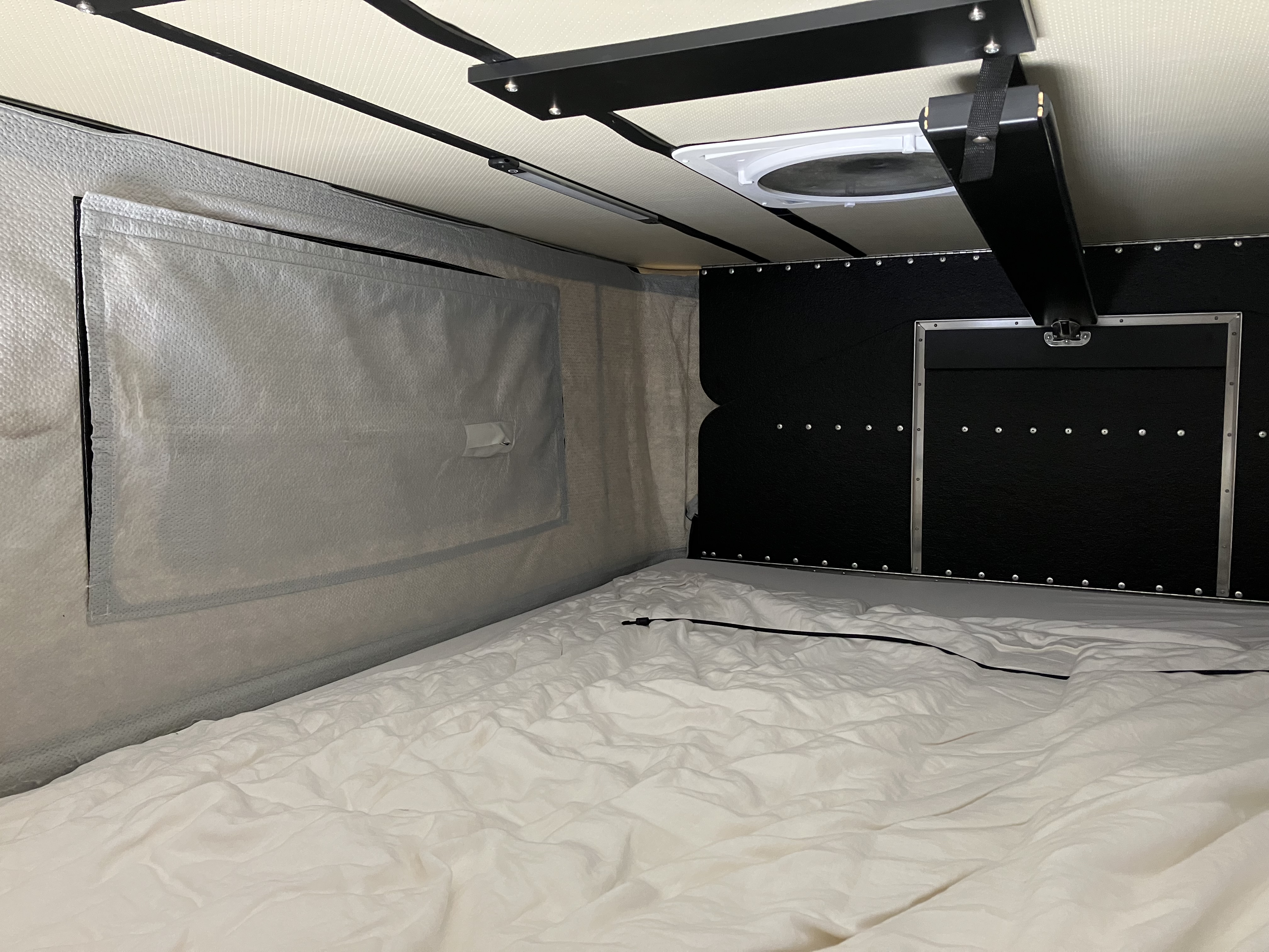 Project M upper sleeping area with custom 5-inch FoamOrder mattress, Ocochi bedding, the FWC interior insulation kit visible on the left wall, and the ceiling fan overhead