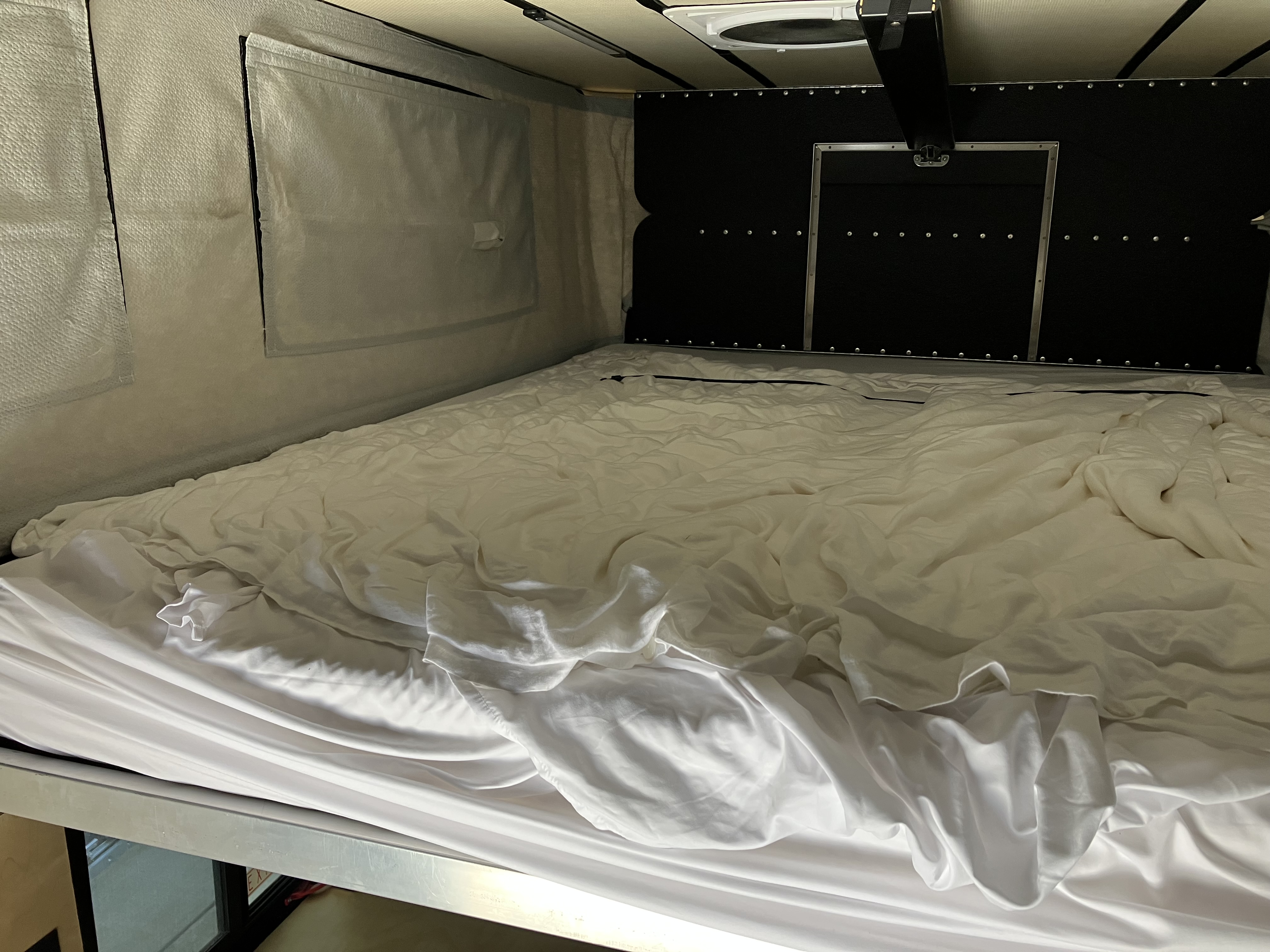 Wide view of the upper bed in the Project M showing the custom queen-plus mattress, layered bedding, and FWC insulation lining the side walls